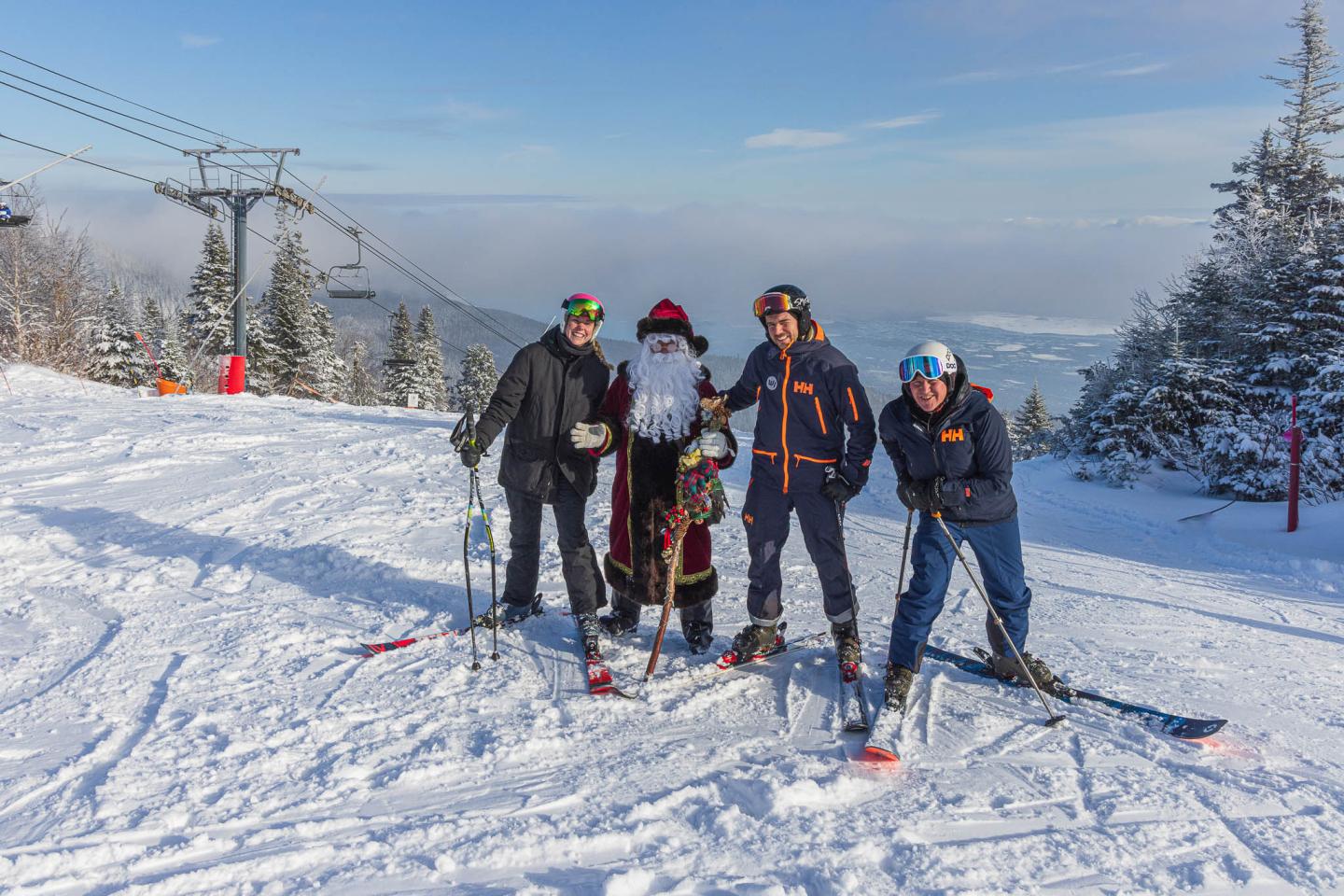Quatre skieurs posent sur une piste enneigée, montagnes en arrière-plan.