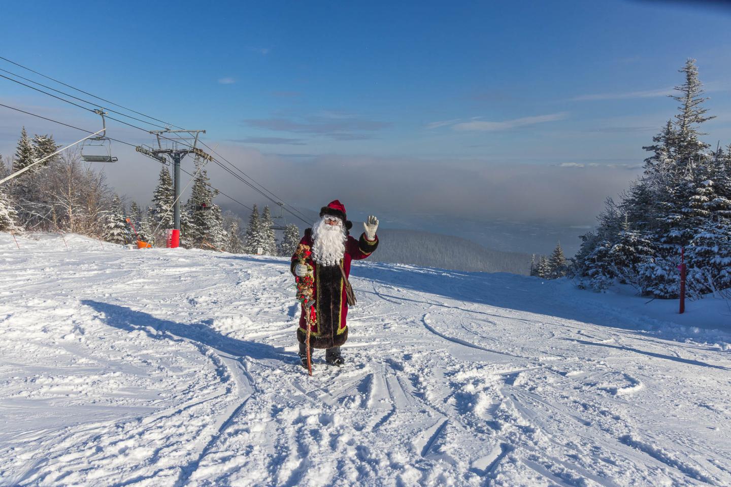 Skieur en tenue rouge et noire saluant sur une piste enneigée.