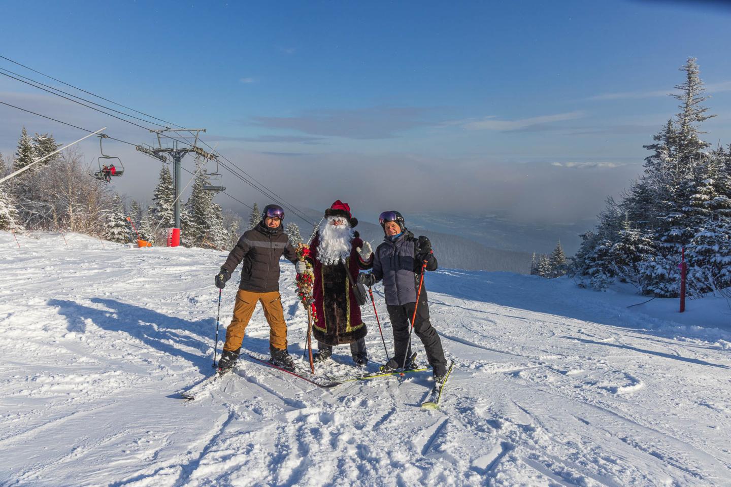 Trois skieurs posent sur une piste enneigée sous un ciel bleu.