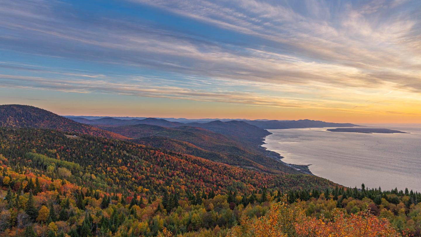 Vue panoramique d’une forêt automnale, collines et lac au coucher du soleil.