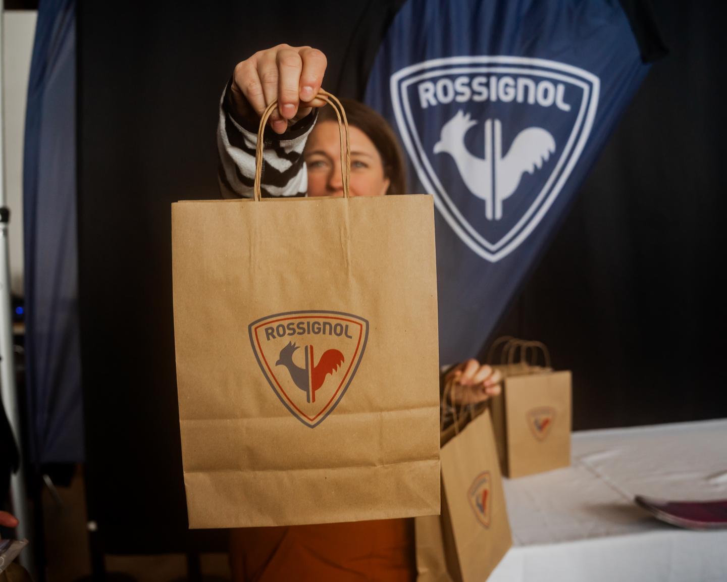 Sac en papier Rossignol tenu devant un logo de la marque.