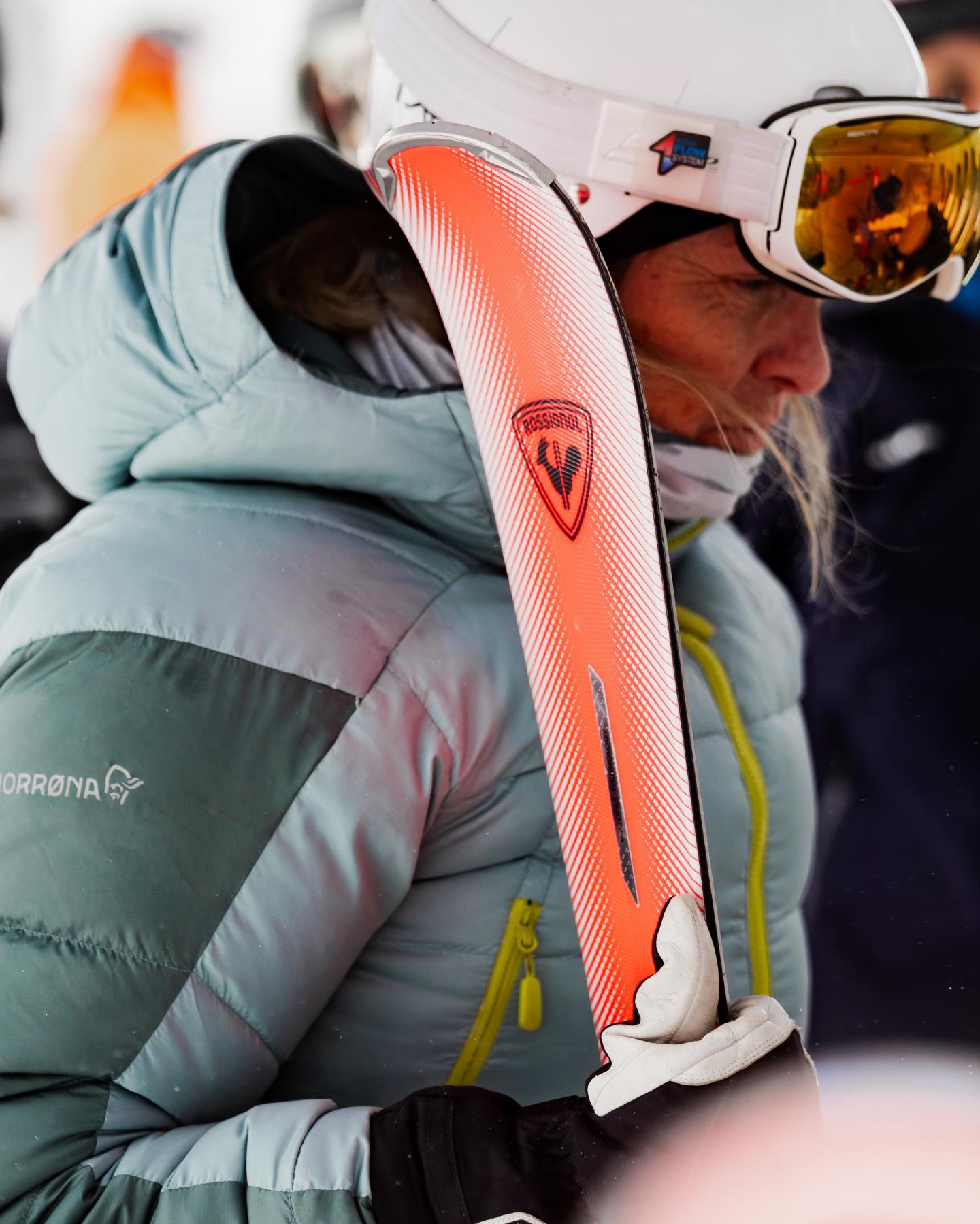 Skieuse en doudoune blanche tenant un ski orange enneigé.
