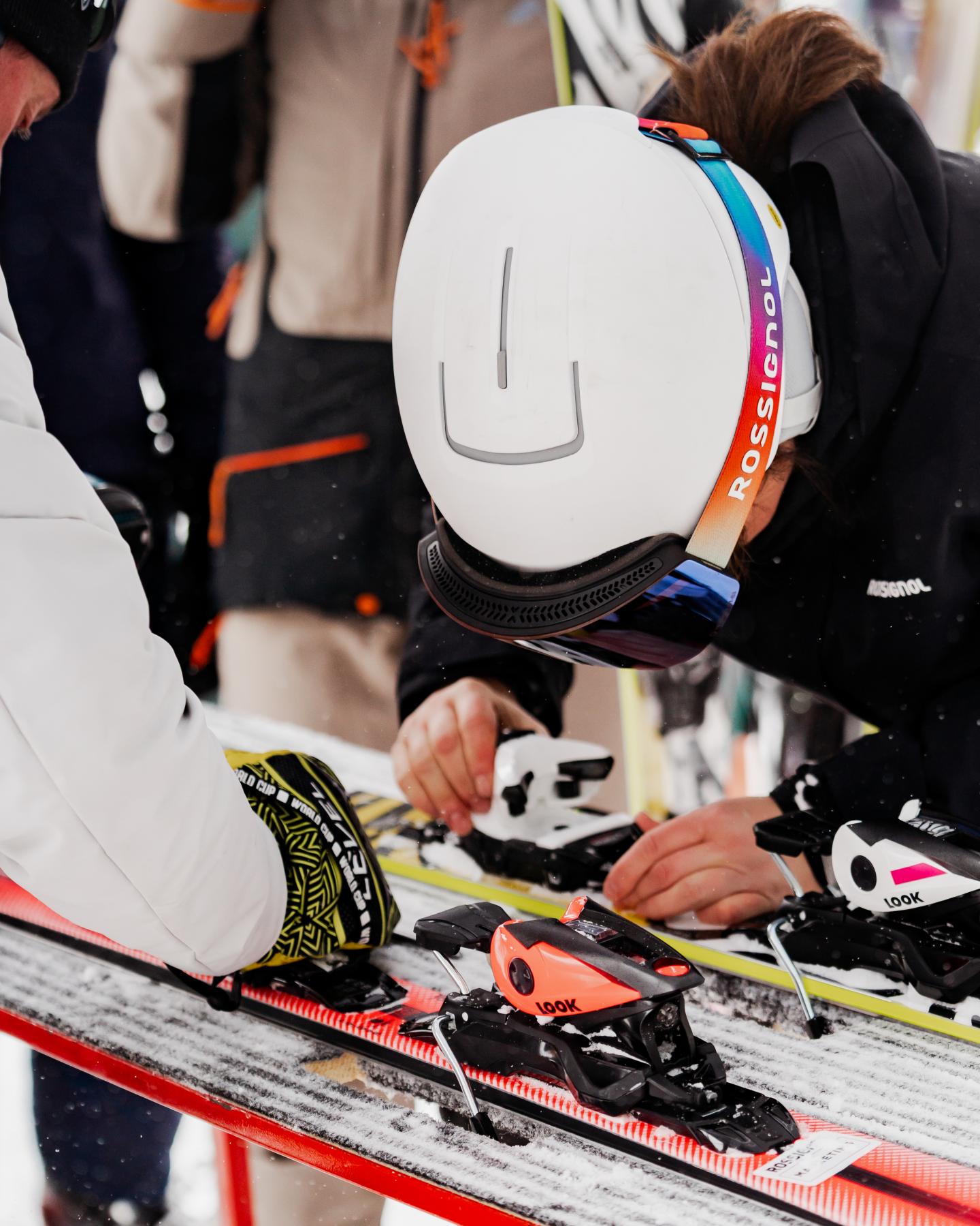 Skieuse en casque blanc ajustant ses fixations sur des skis.