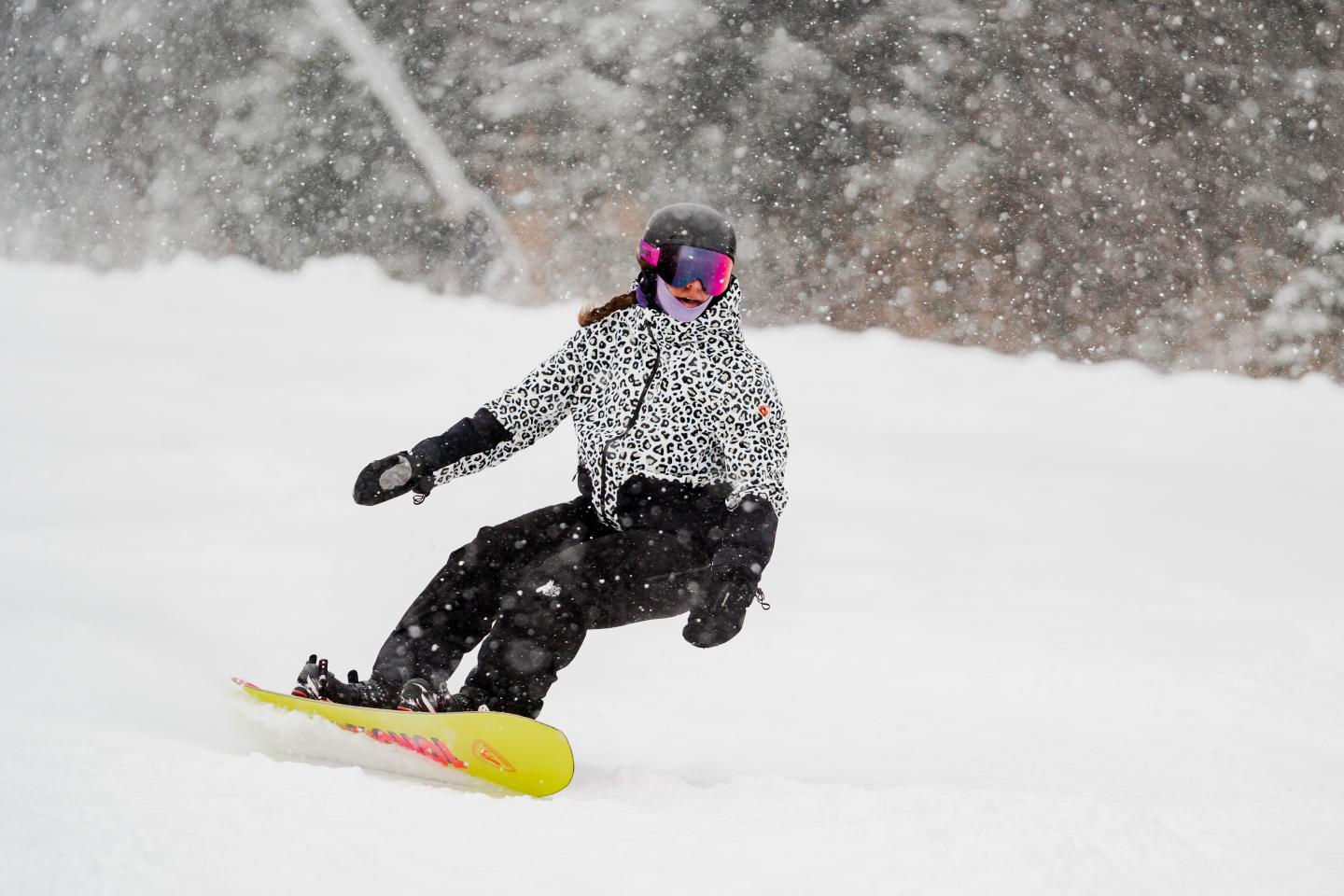 Snowboardeur en tenue noire dévalant une piste enneigée sous une forte chute de neige.