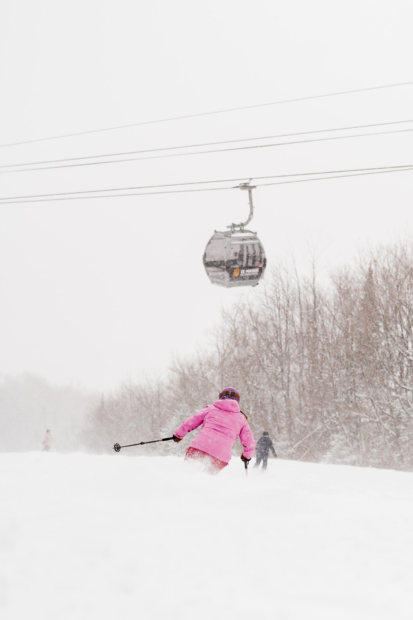 Skieuse en rose dans la neige, sous une télécabine.