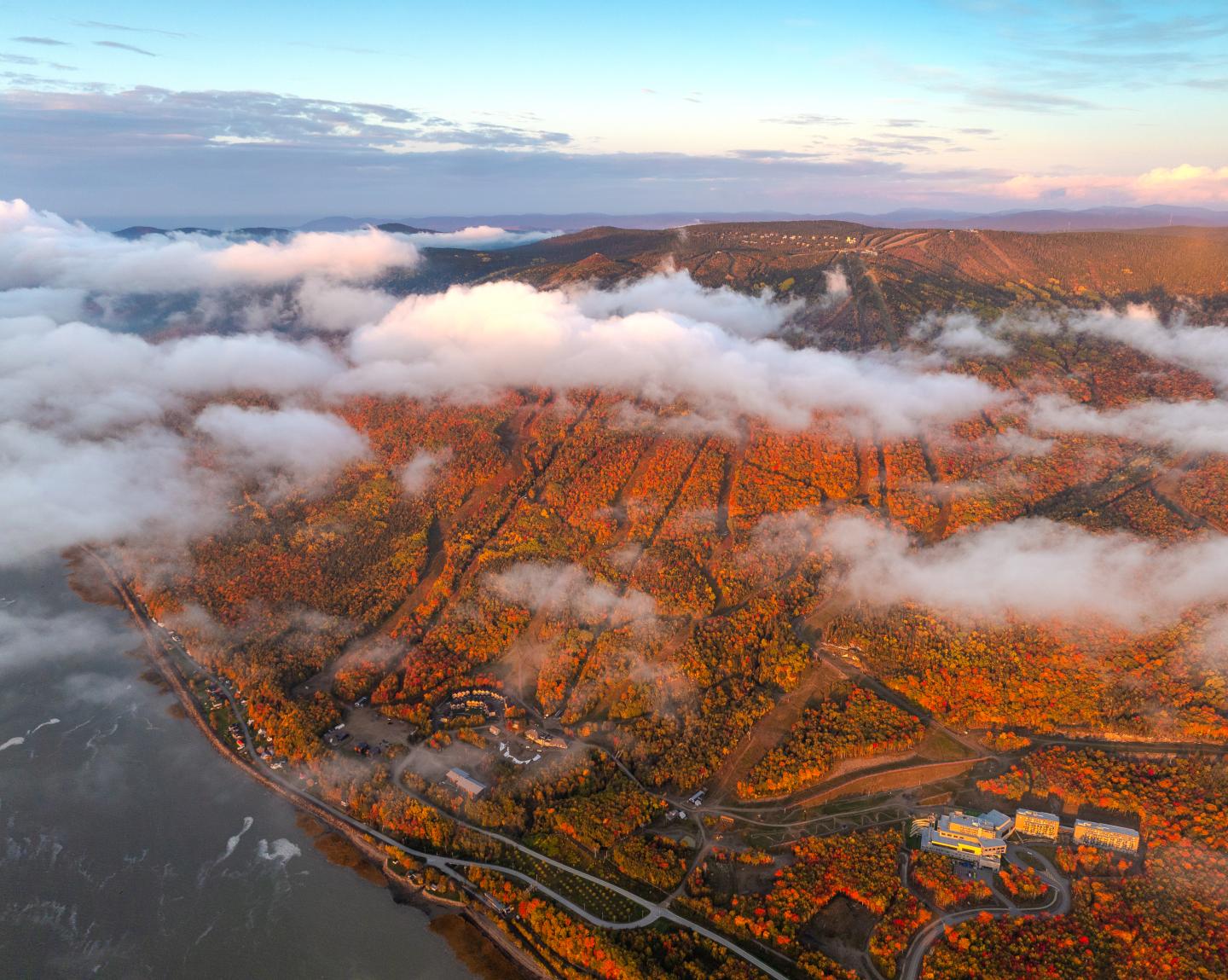 Vue aérienne d’un littoral montagneux au coucher du soleil, couvert de nuages bas.