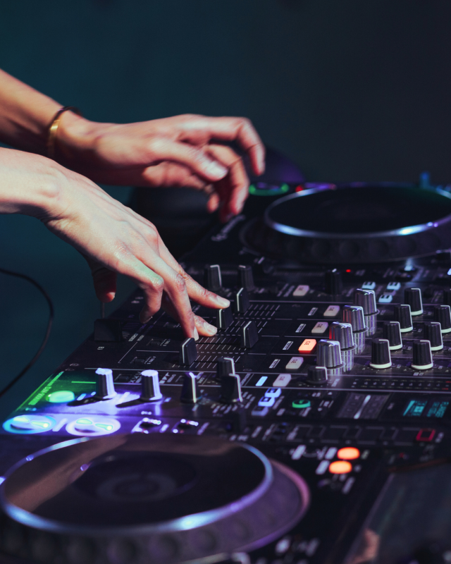 Mains manipulant une table de mixage DJ éclairée en violet et bleu.