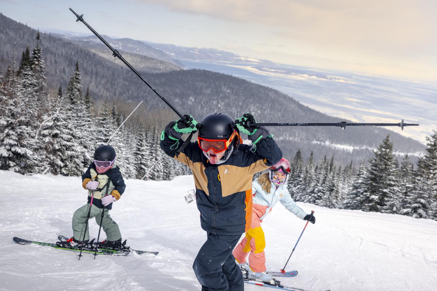 Skieurs dévalant une piste enneigée bordée de sapins et de montagnes.