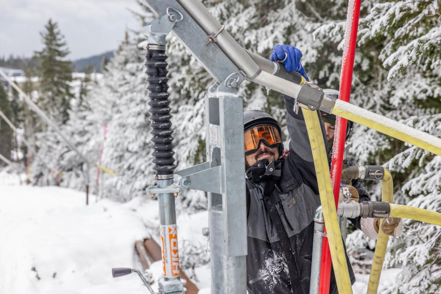 Technicien en hiver inspectant un équipement électrique près de câbles jaunes.