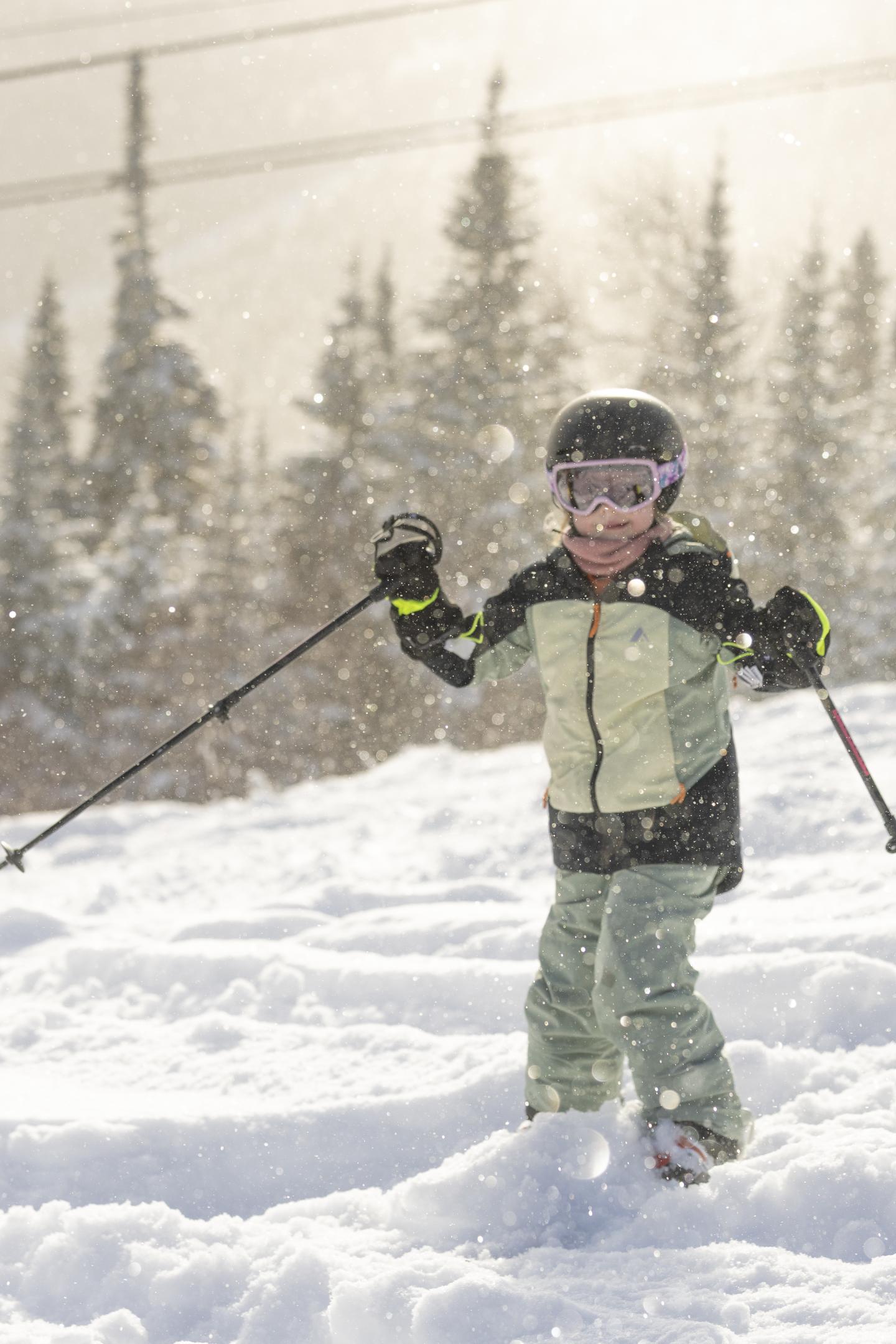 Enfant en tenue de ski tenant des bâtons dans la neige.