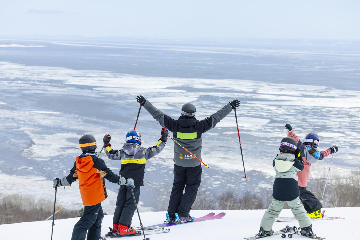 Skieurs au sommet enneigé, bras levés face aux montagnes.