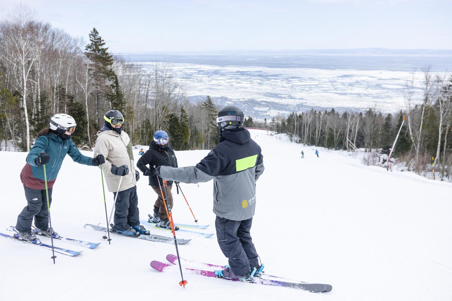 Skieurs équipés au sommet d’une piste enneigée, vallée brumeuse en arrière-plan.