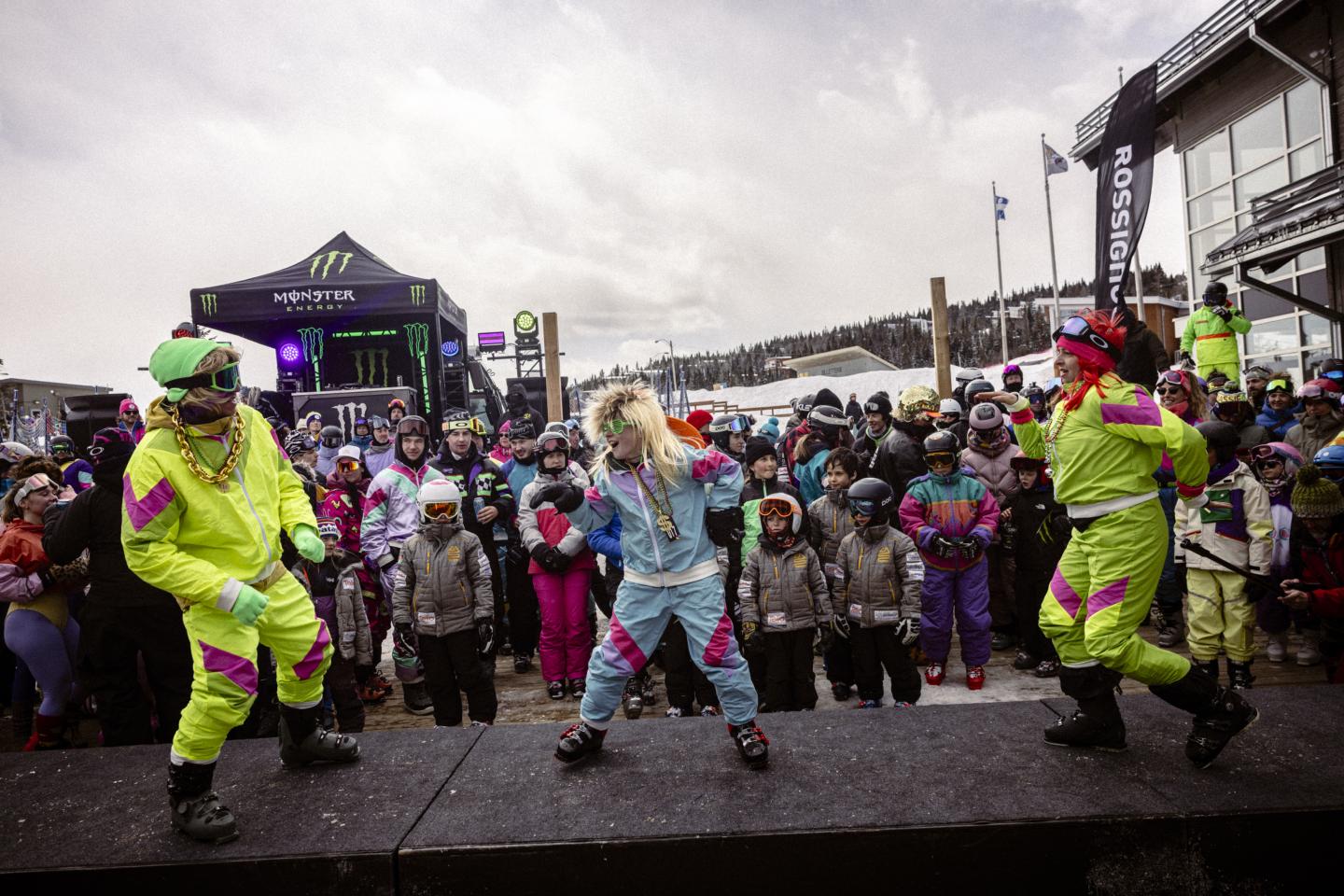 Parade colorée sous la pluie, avec danseurs en costumes fluo devant une foule.