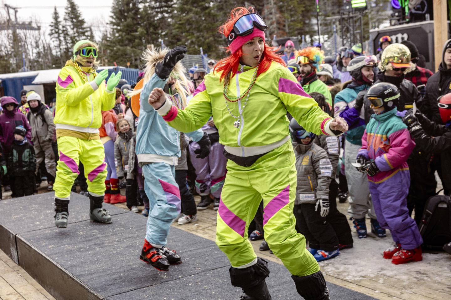 Carnavaliers en costumes fluo dansant dans une rue sous la pluie.