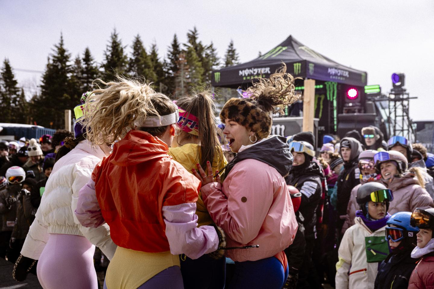 Deux femmes enlacées dans une foule devant une scène de festival.