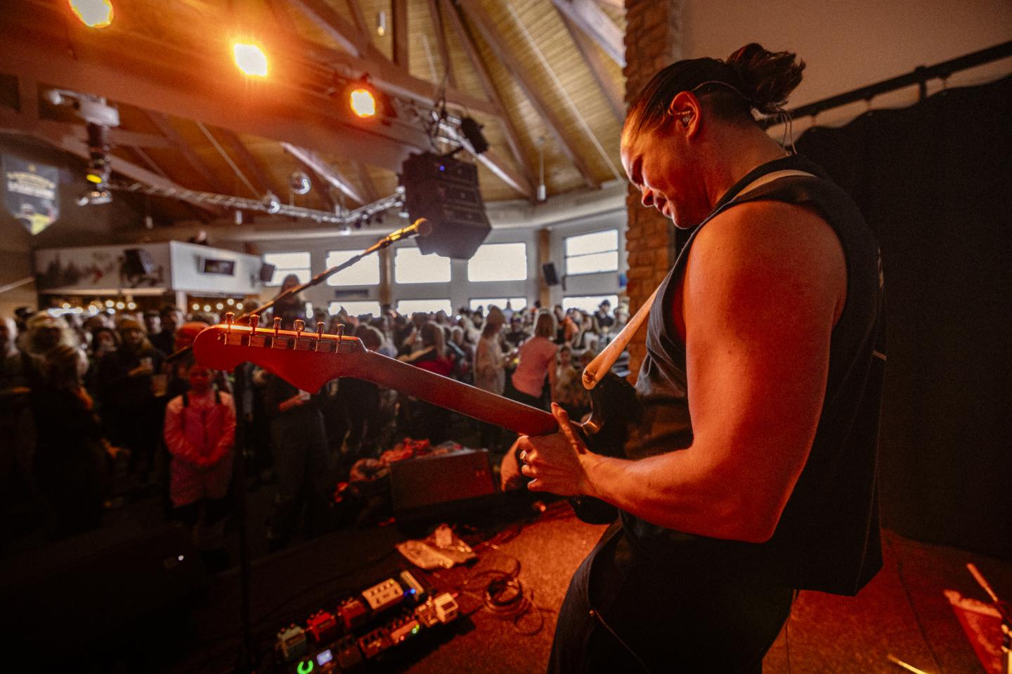 Guitariste sur scène, éclairé en orange devant une foule.