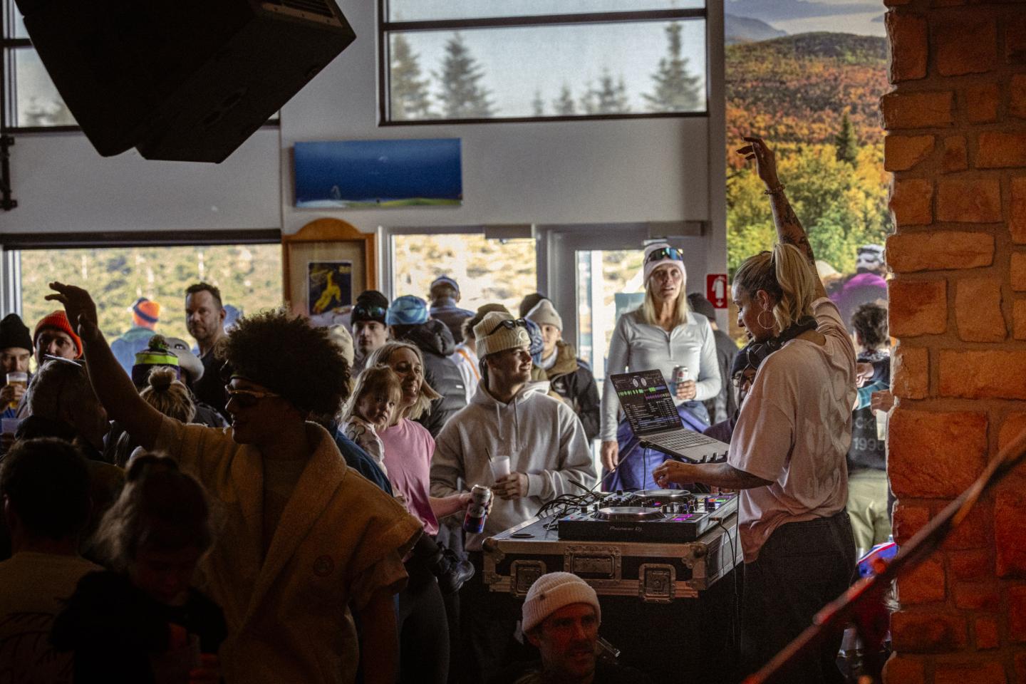 Foule dans un café rustique, près de grandes fenêtres donnant sur les montagnes.