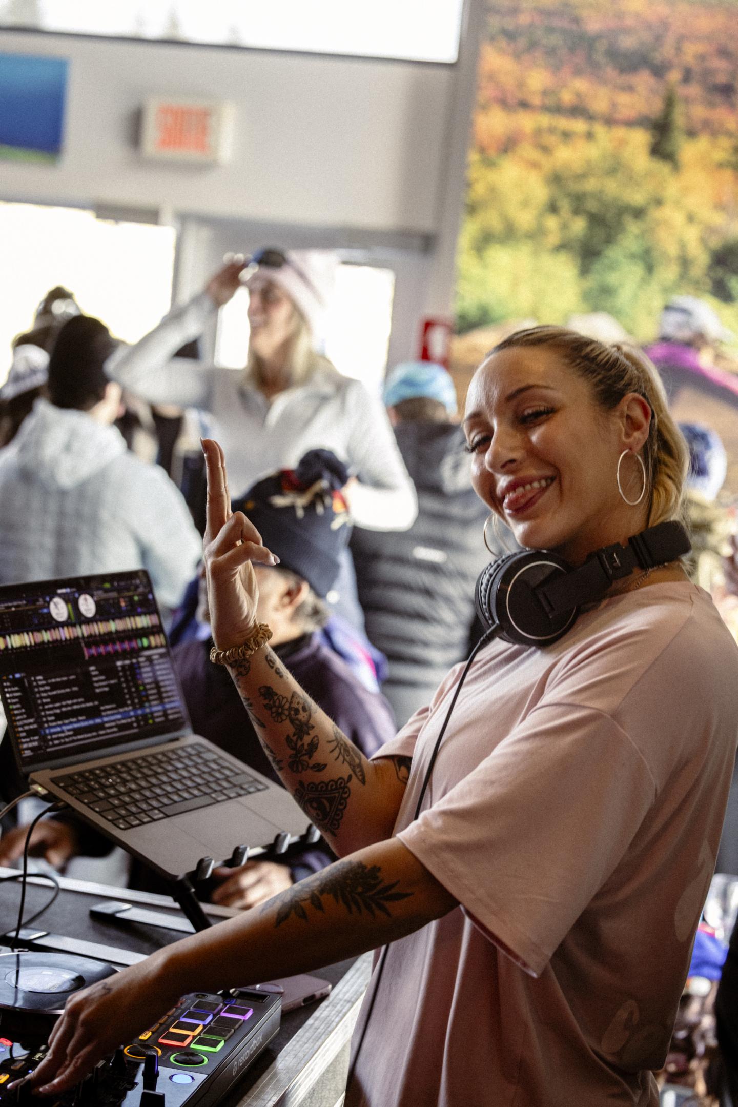DJ souriante avec casque, mixant sur une console devant un public.