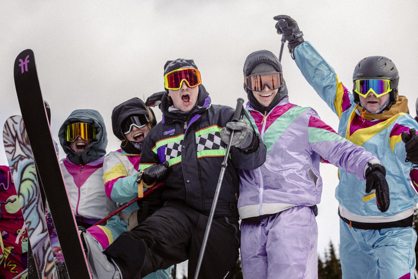 Quatre snowboardeurs en tenues colorées posent avec leurs planches dans la neige.