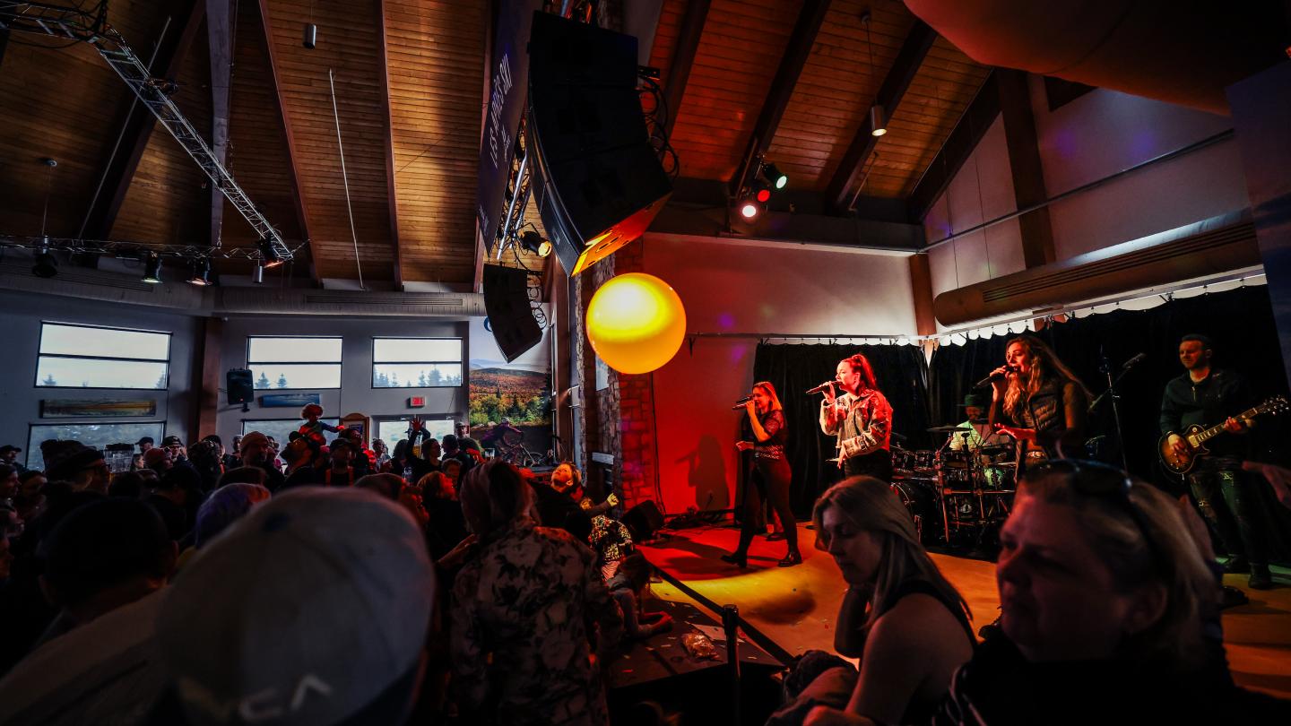Concert sur une petite scène, éclairé en rouge et jaune, devant une foule.