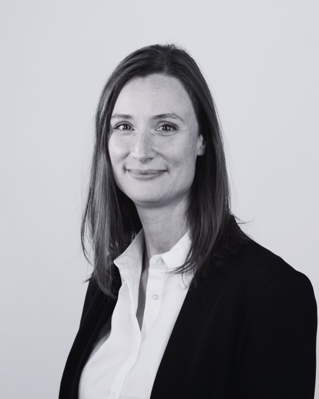 Portrait professionnel d’une femme souriante en blazer noir et chemise blanche.