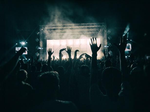 Foule en silhouette levant les bras devant une scène éclairée lors d’un concert.