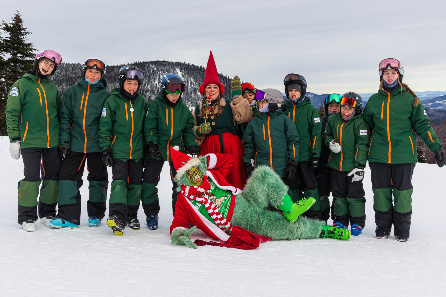 Équipe de ski en vestes vertes posant avec un drapeau rouge sur la neige.