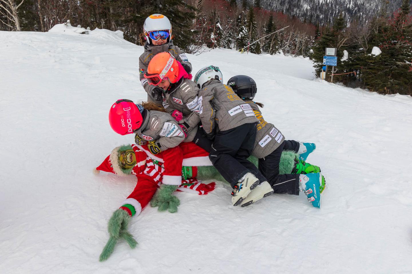 Enfants casqués jouant dans la neige avec des luges colorées.