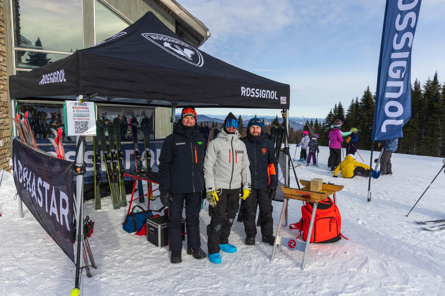 Stand Rossignol sur la neige, avec skis, bottes et skieurs en tenue d’hiver.