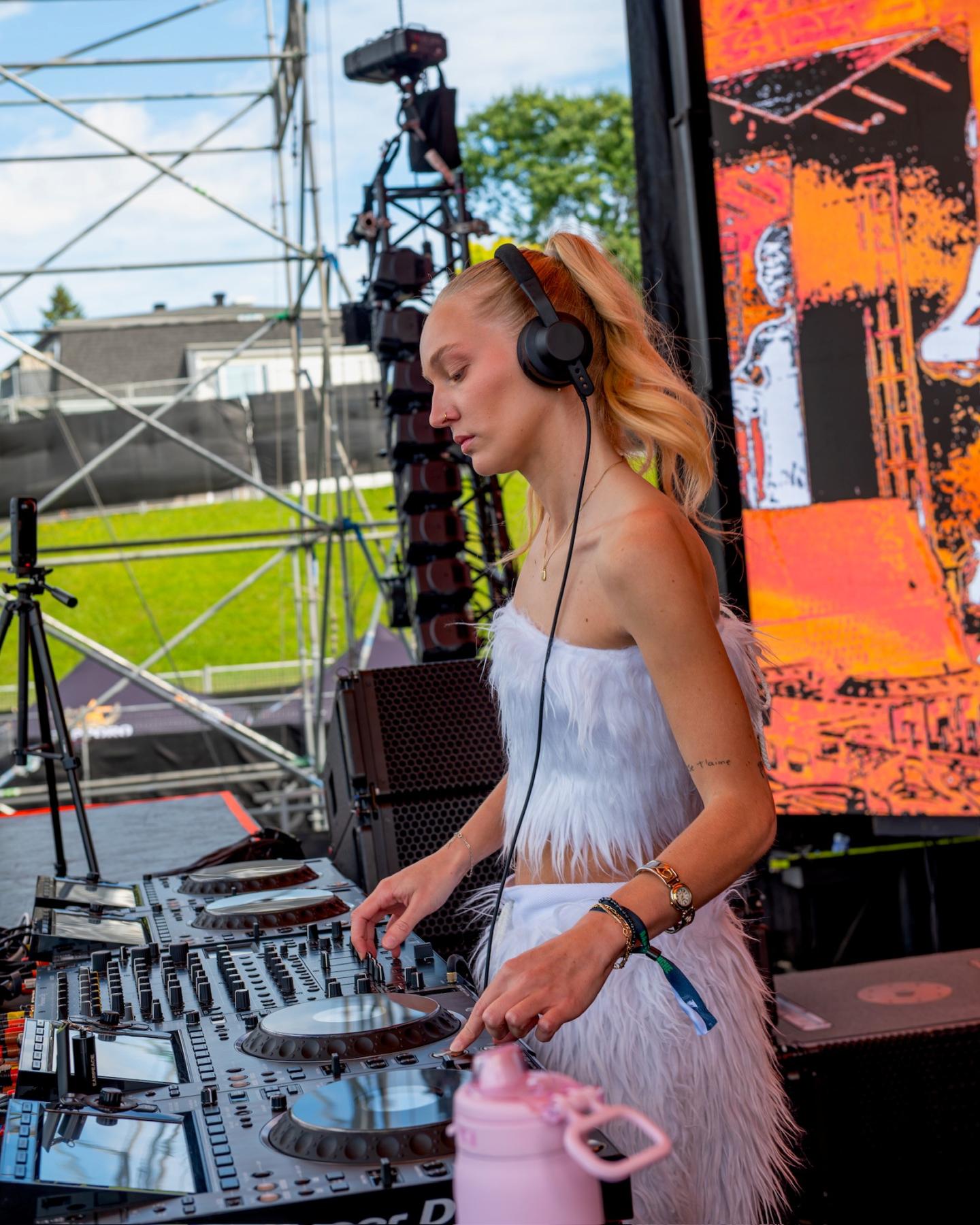 DJ femme mixant sur une console en plein air, devant un écran orange.