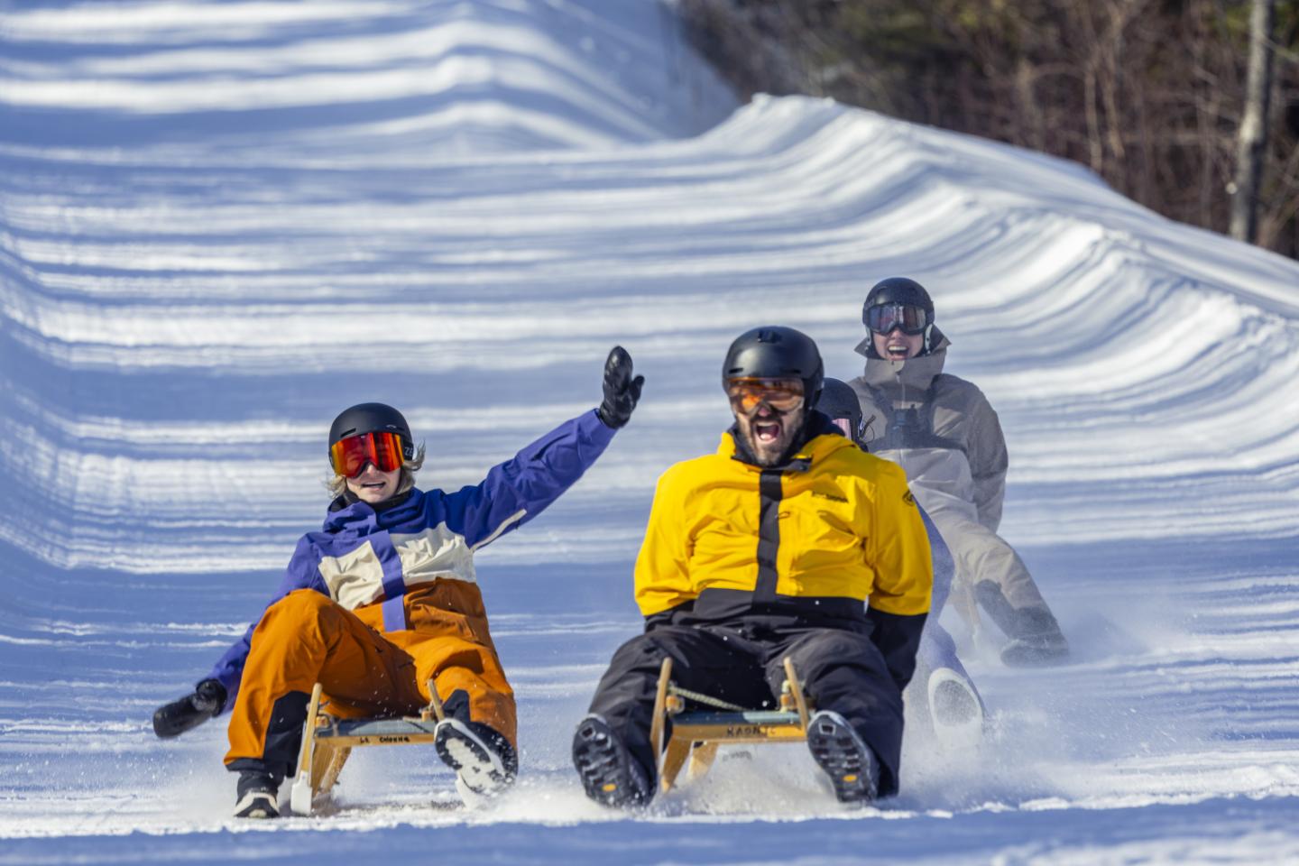 Deux snowboardeurs descendent une piste enneigée, un troisième suit derrière.